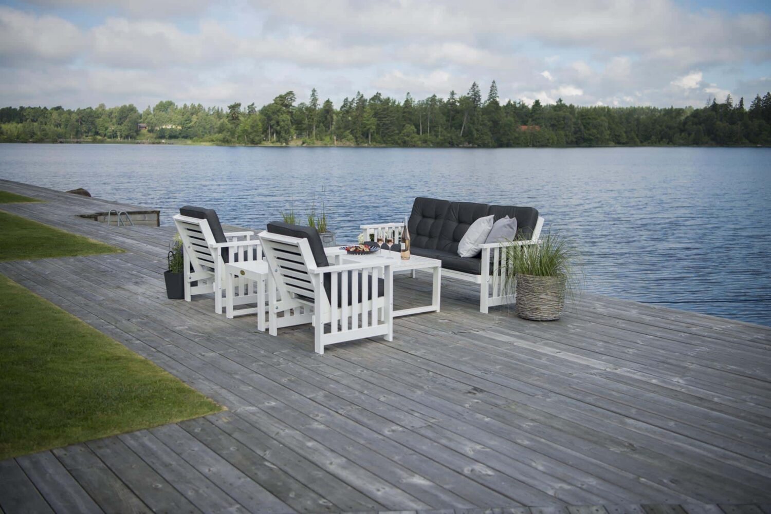 Hillerstorp Gotland Loungegrupp vit. Gruppen består av 3-sitssoffa, två fåtöljer och loungebord. På bilden med mörkblå dynor.